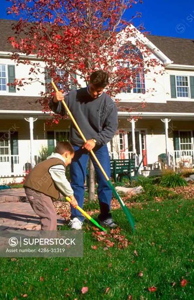 Father and his young son raking fall leaves together in front of their home.