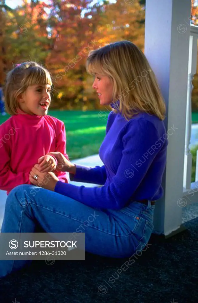 Mother and her young daughter sitting on the porch and talking together.