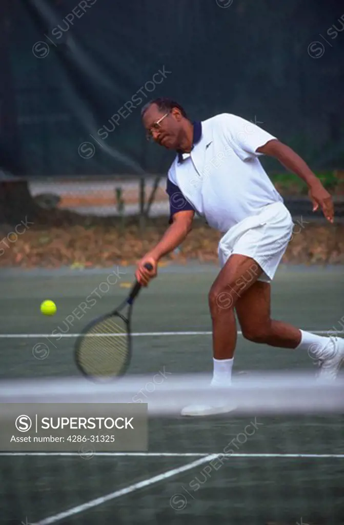 Senior African American man lunging for the ball while playing tennis.