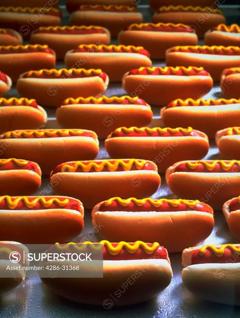 Still life of several hot dogs in buns with mustard.