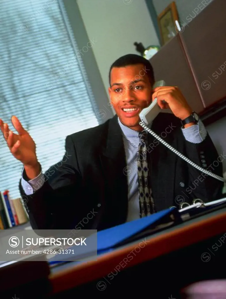A young African American business executive sitting at a desk talking on the phone.