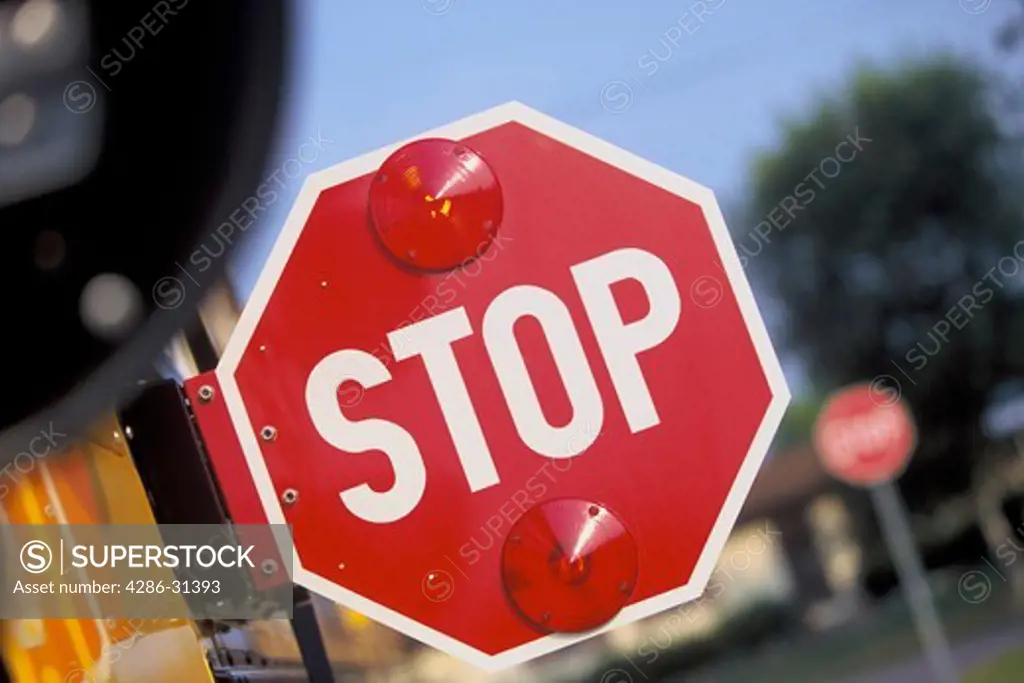 Close-up of a stop sign that is extended from a school bus as it is stopped and children  cross the street. 