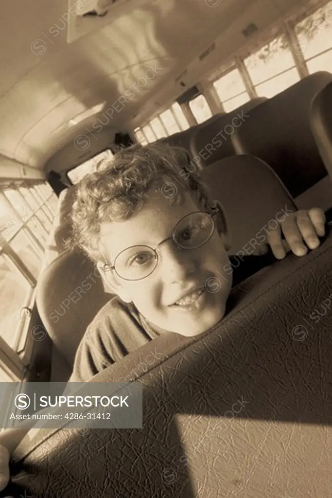 Black and white close-up of a child leaning forward on a bus seat resting his chin on the backrest. 