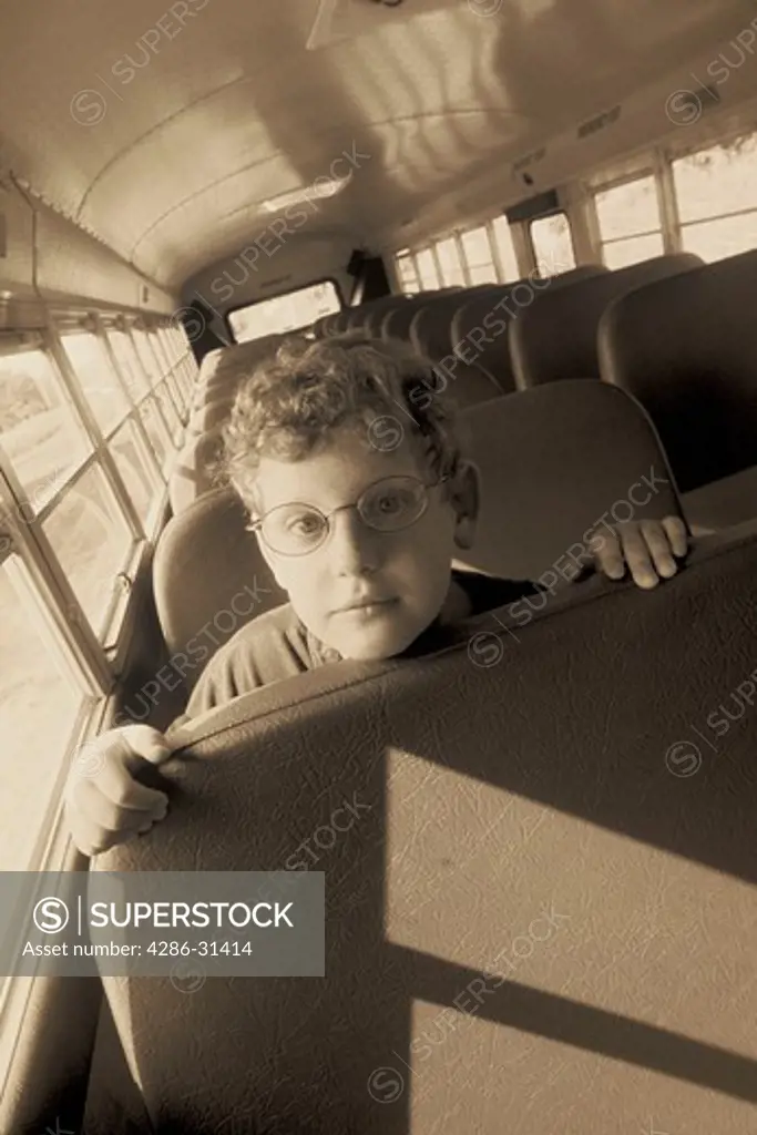Black and white close-up of a child leaning forward on a bus seat looking disappointed or sad. 