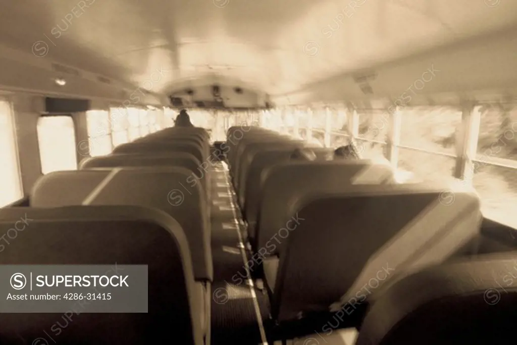 Black and white inside shot of the length of an entire school bus with a few blurred children in the bus.