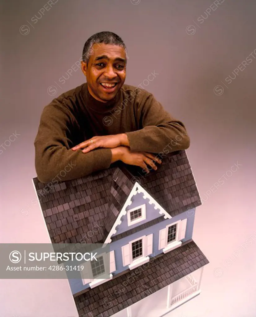 Portrait of an African-American man leaning against a model home symbolizing banking and home mortgages.