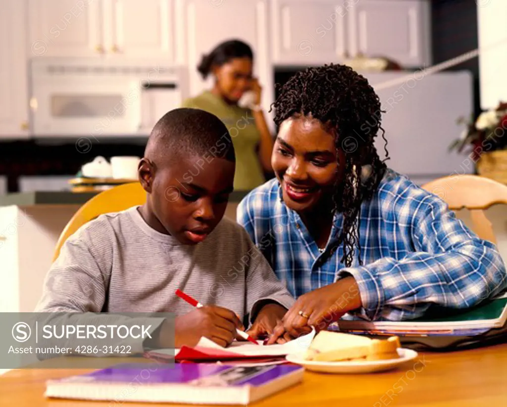 Close-up of African-American mother and son sitting at the dinner table working on his homework. 