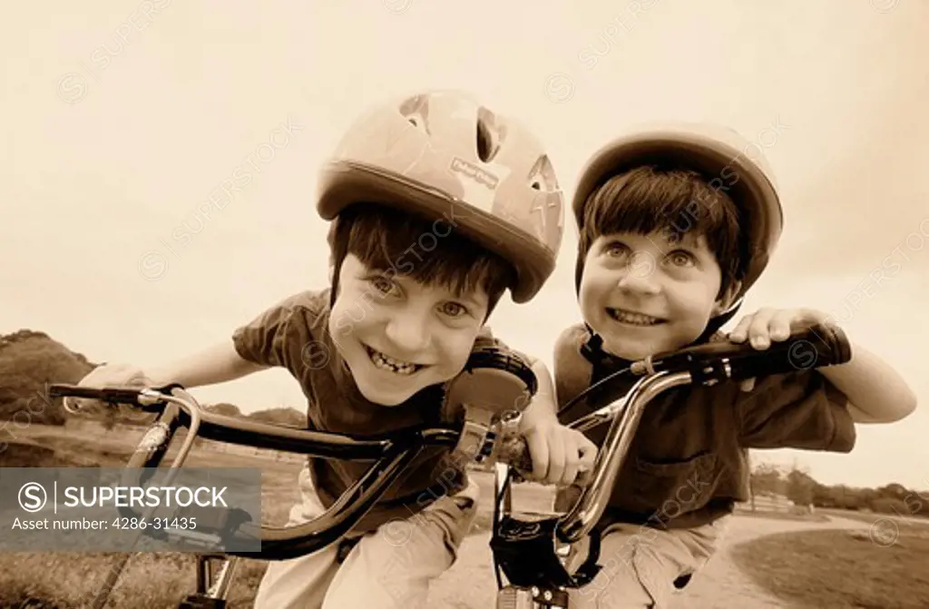 Close-up of twin boys who are wearing helmets while riding their bicycles.