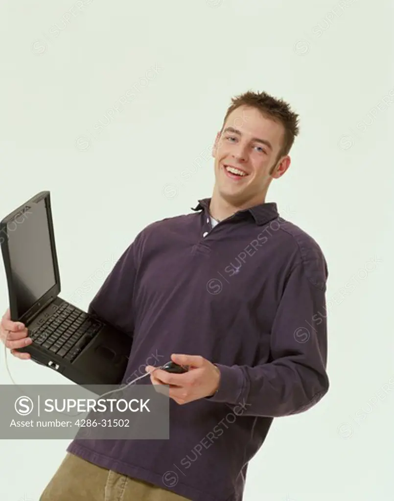 Studio portrait of a smiling male teenager holding a black laptop computer and an attached mouse