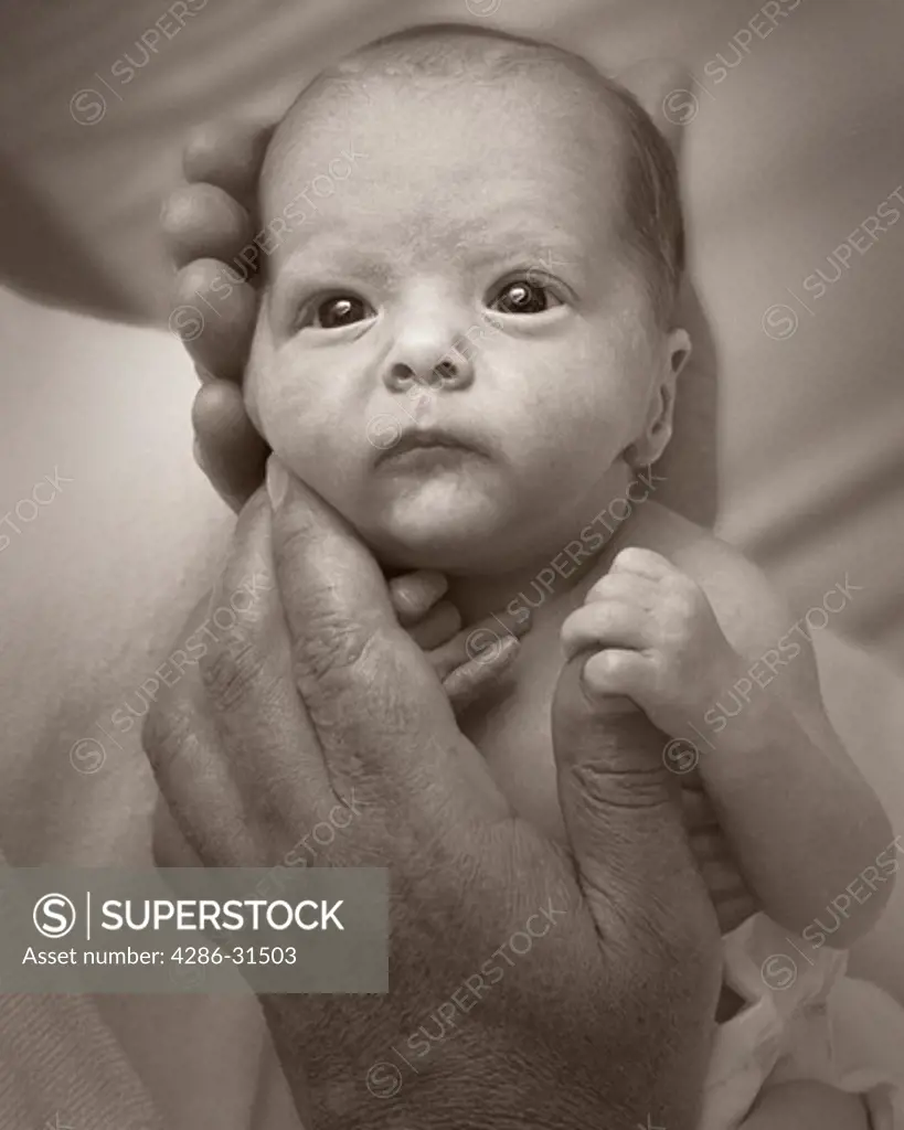 Close-up portrait of a newborn baby being held in an adult mans hands.