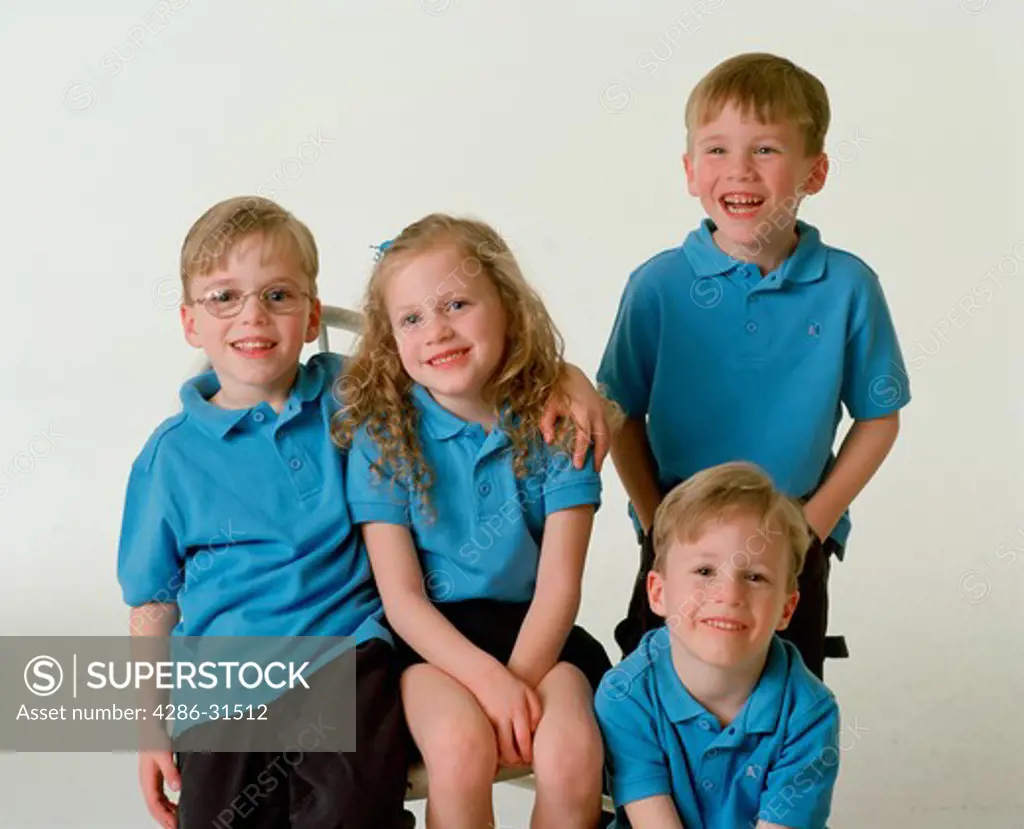 Studio portrait of quadruplets, three boys and a girl, wearing matching blue shirts.