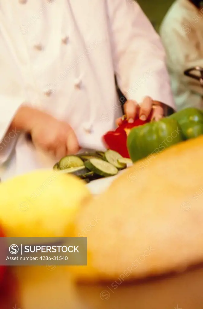 A chef prepares food at a restaurant, cutting cucumbers and peppers amongst other vegetables. 