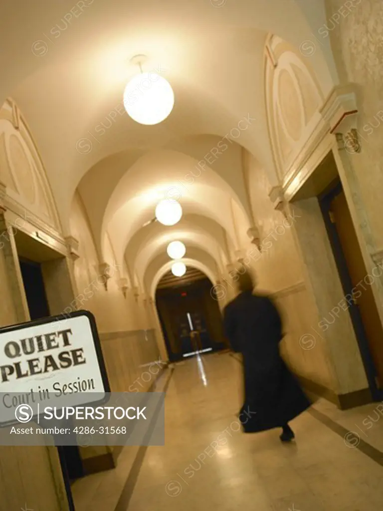 Blurred vertical images of a judge walking down a hallway in a courthouse.