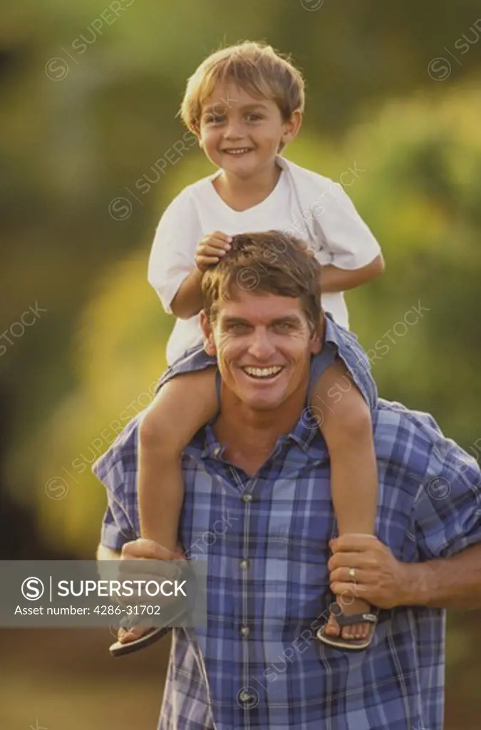 Portrait of a smiling father carrying his happy son on his shoulders outdoors.