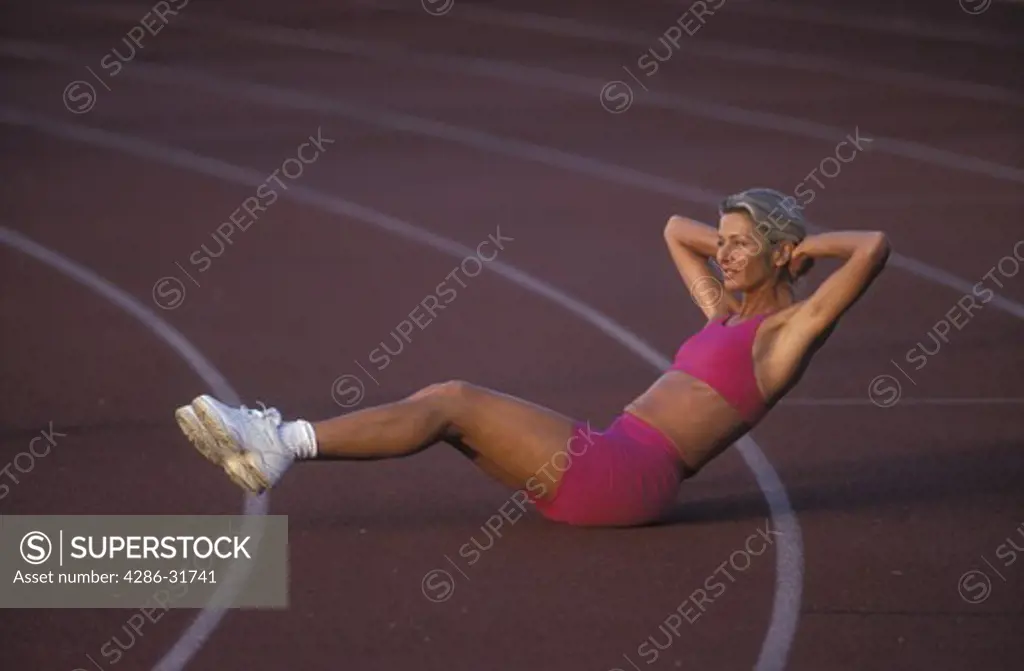 Woman does stretching sit-ups on an outdoor track.