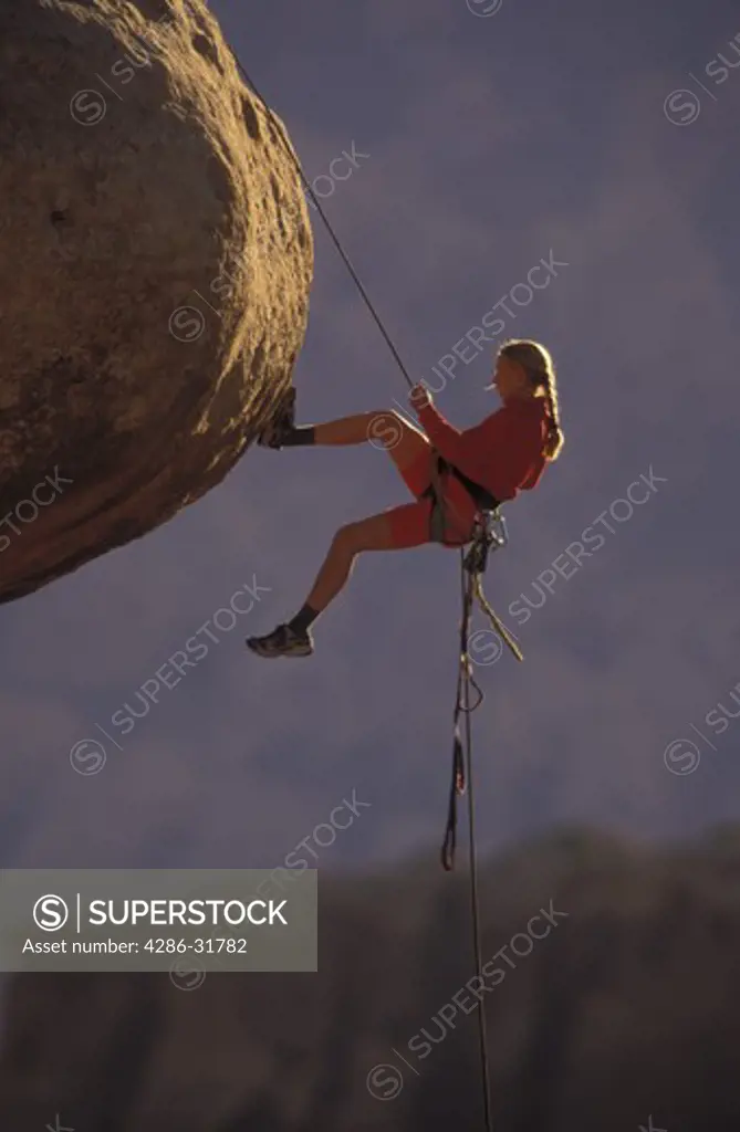 Female climber about to rappel off a jutting outcrop of rock.