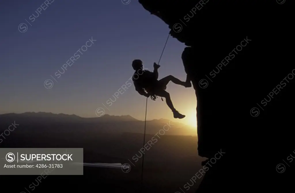 Silhouette of a mountain climber rappelling down a sheer cliff.