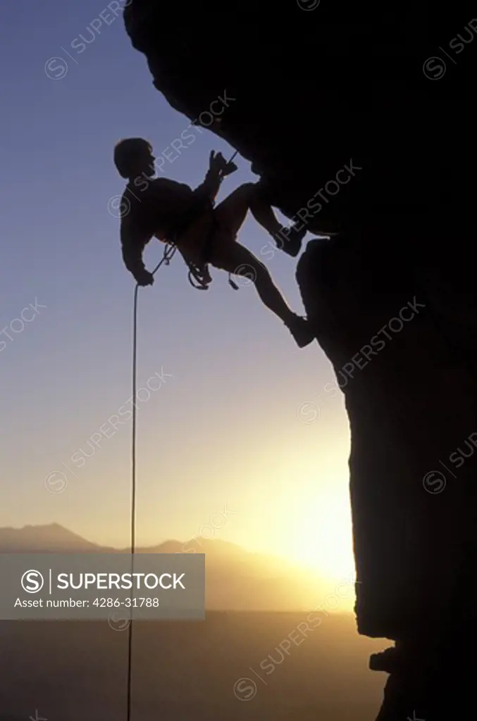 Silhouette of a mountain climber rappelling down a cliff.