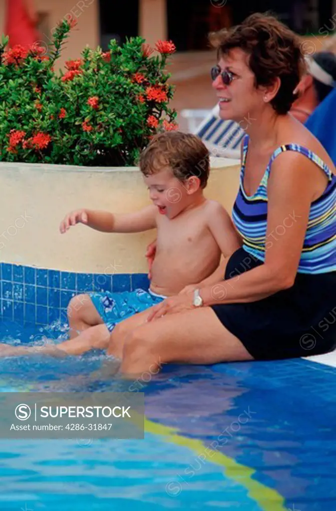 Grandmother and grandchild sitting by the edge of the pool. 