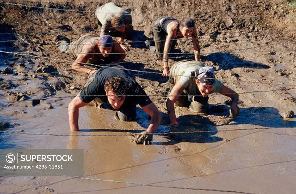 Group of people army crawling on their bellies under steel wires through the mud. 
