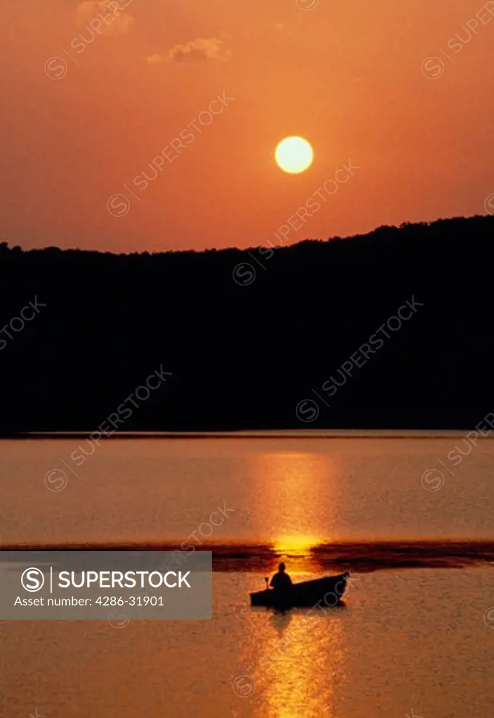 Silhouette of man fishing from boat at sunset in Devils Lake State Park, Wisconsin.