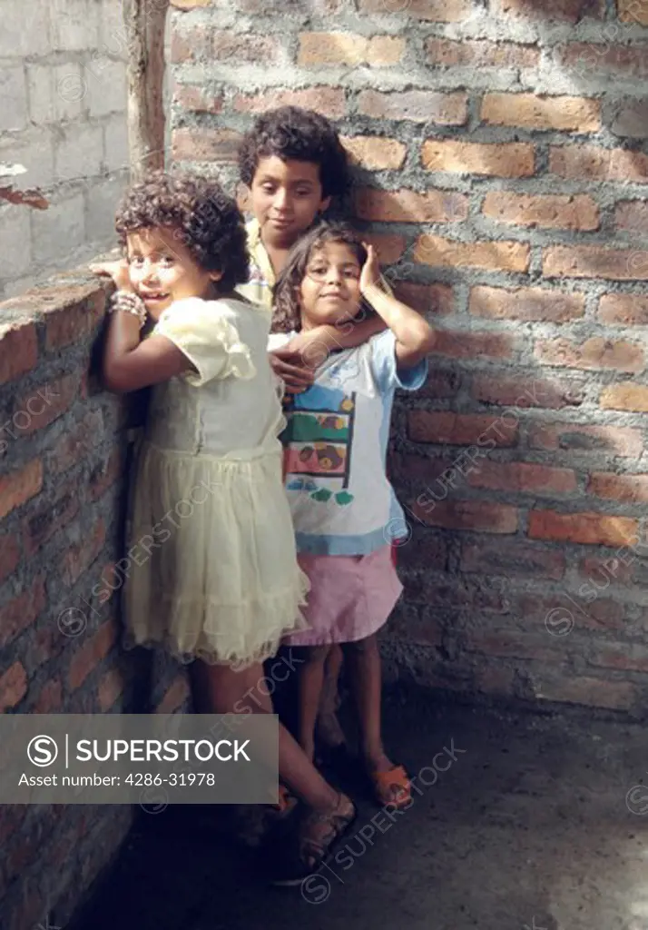 A trio of Nicaraguan children standing inside a brick structure as sunlight shines in from a window.