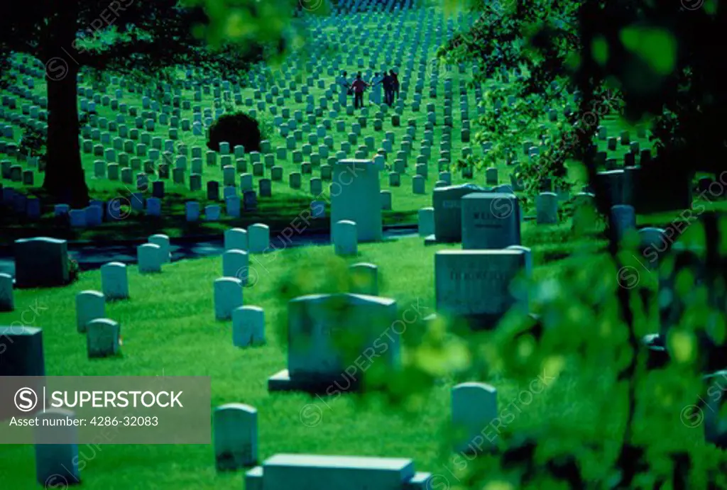 Headstones at Arlington National Cemetery. In the background a family gathers around a gravesite.