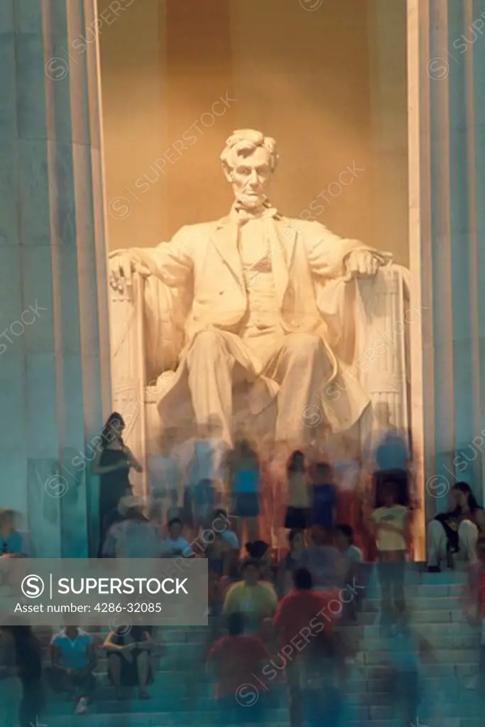 The statue of Abraham Lincoln in his Memorial gazes down upon time-blurred tourists in the early evening light.