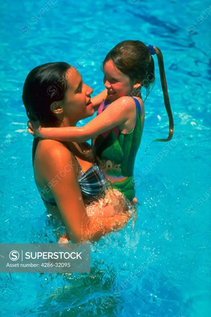 Teenage 13-year-old girl holding a younger 6-year-old girl while playing in a swimming pool.