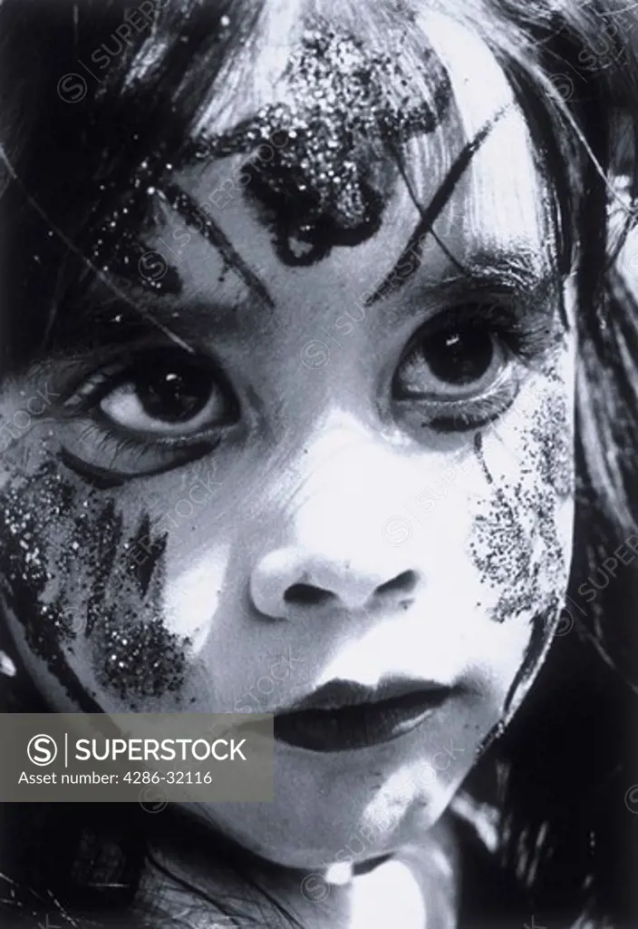 Close-up portrait of a young girl with her face painted with clown make-up and glitter.