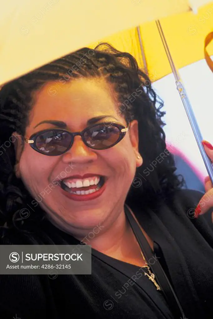 Close-up of an overweight, Hispanic/African-American woman holding an umbrella providing shade. 