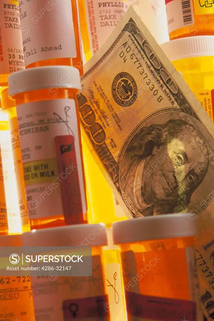 Multitude of prescription bottles stacked on top of one another with a $100 dollar bill placed between them.