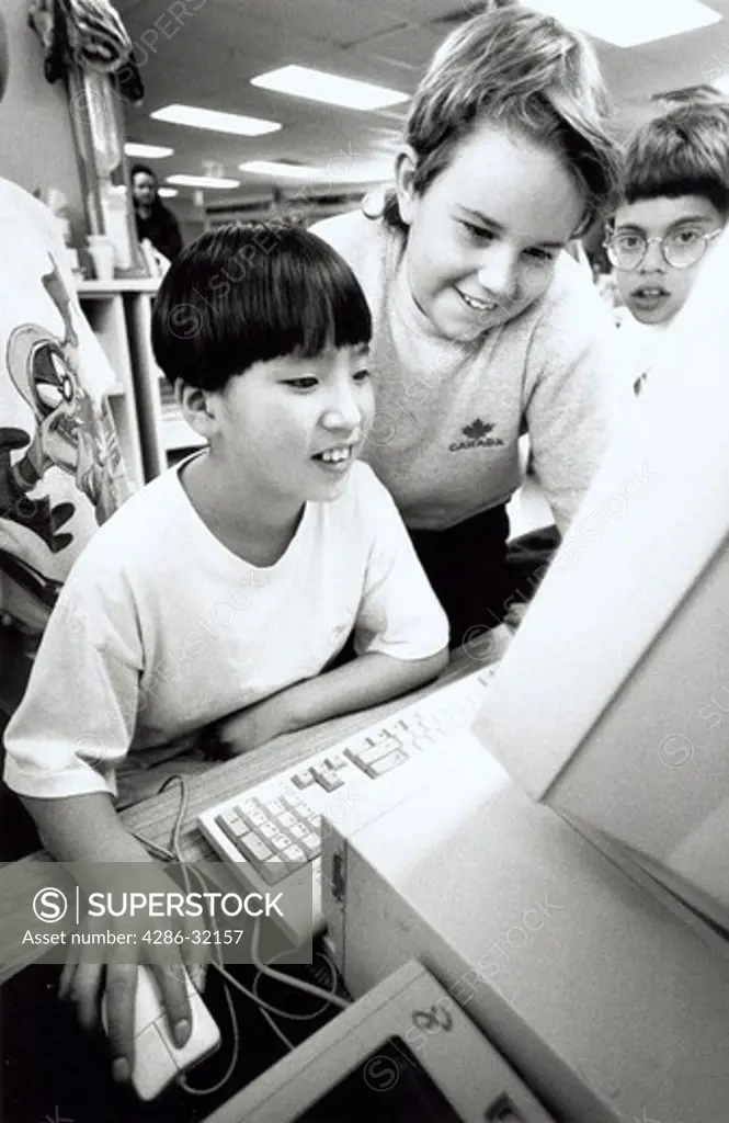 An Asian boy surrounded by other fifth graders as he works on a computer. 