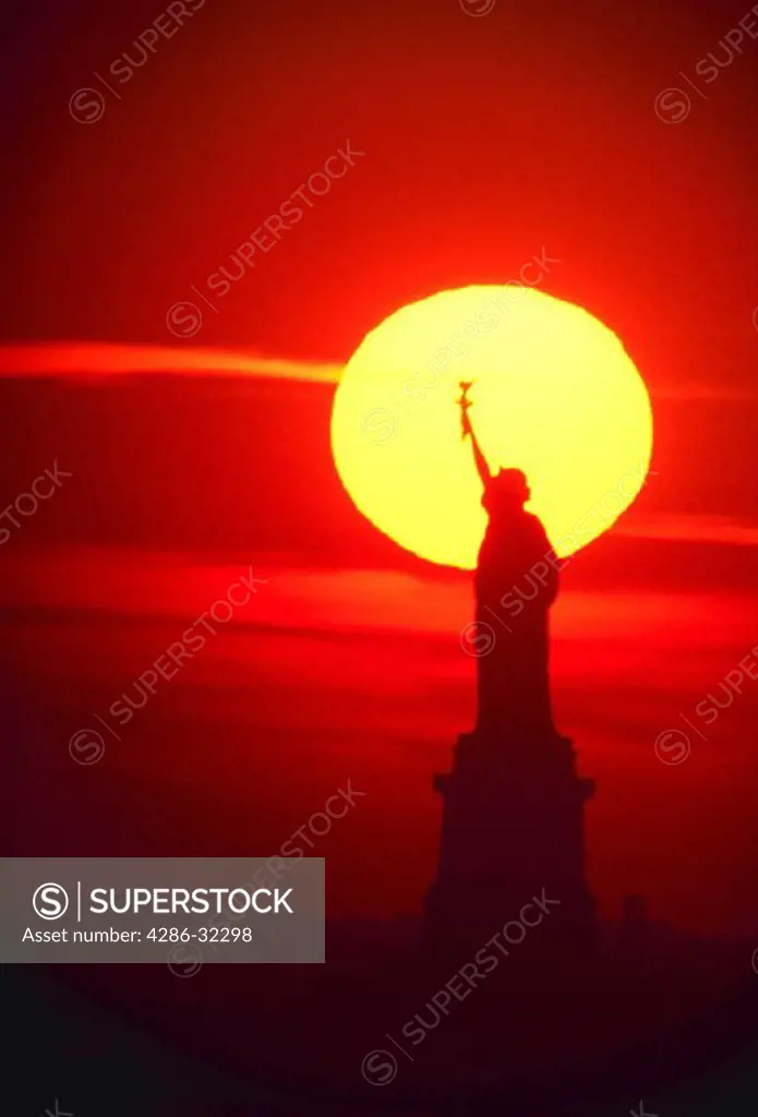 Silhouette of Statue of Liberty against sunset.