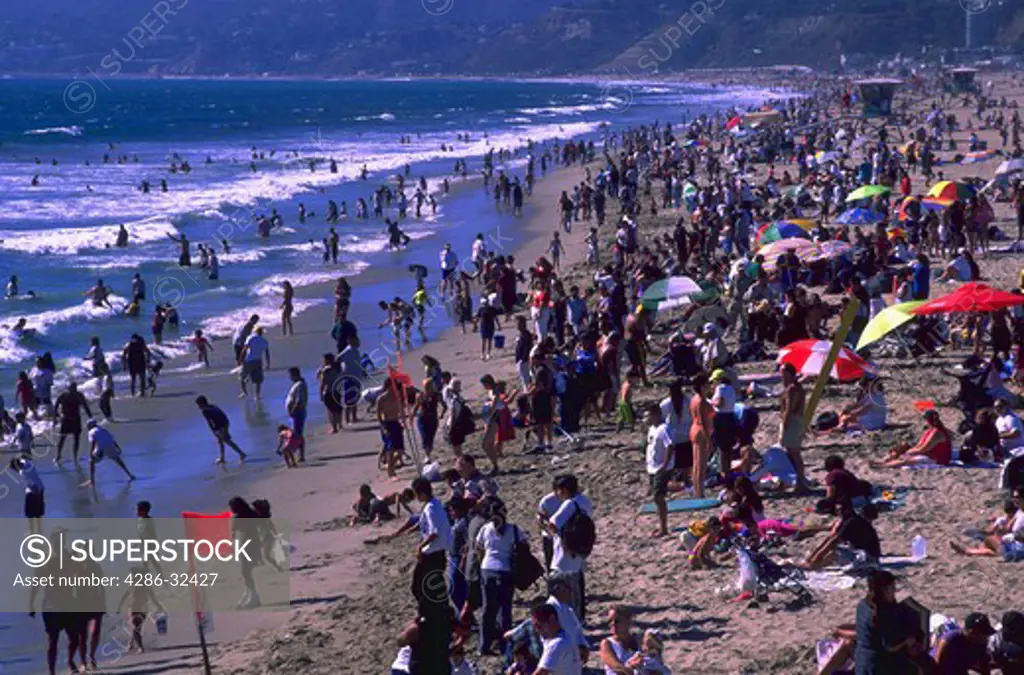 Tourists, sunbather, and swimmers crowd the beach and the water in Santa Monica, California.