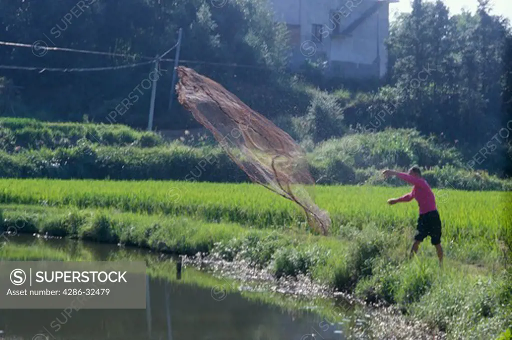 Man casting a fishnet into a pond, Xiangtan, Hunan, China.