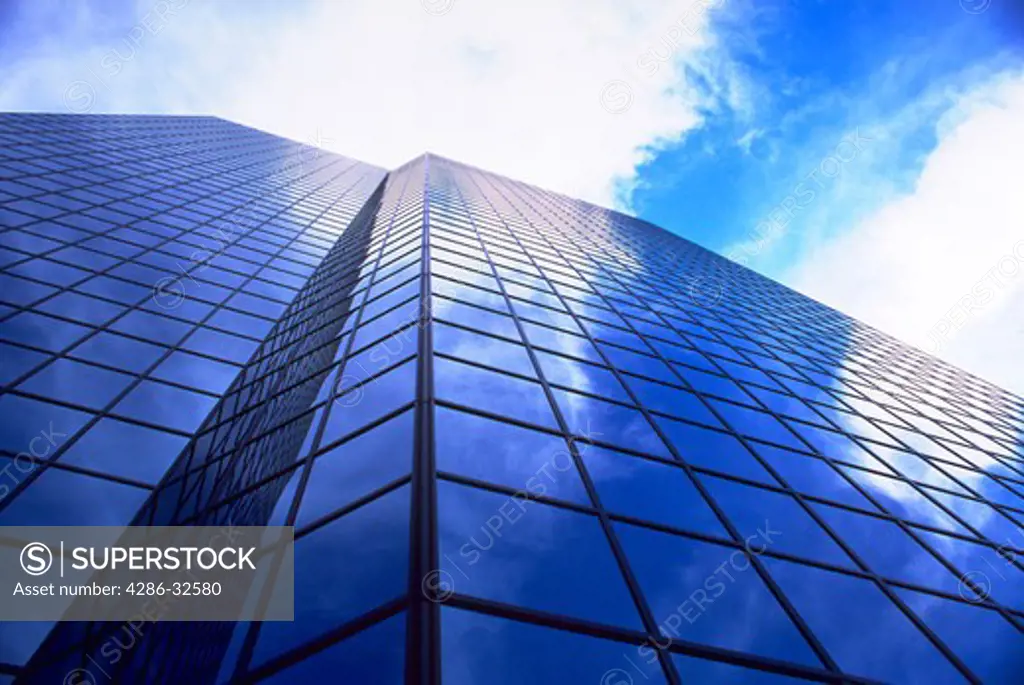 Looking up the side of a corporate office building with cloud reflections on the glass windows.