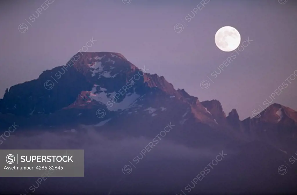 Mood oriented sunset and landscape of full moon over massif of Longs Peak (elevation 14,255 feet) and Keyboard of the Winds in Rocky Mountain National Park (a double exposure photograph, both exposures made with a 350mm lens), Colorado.