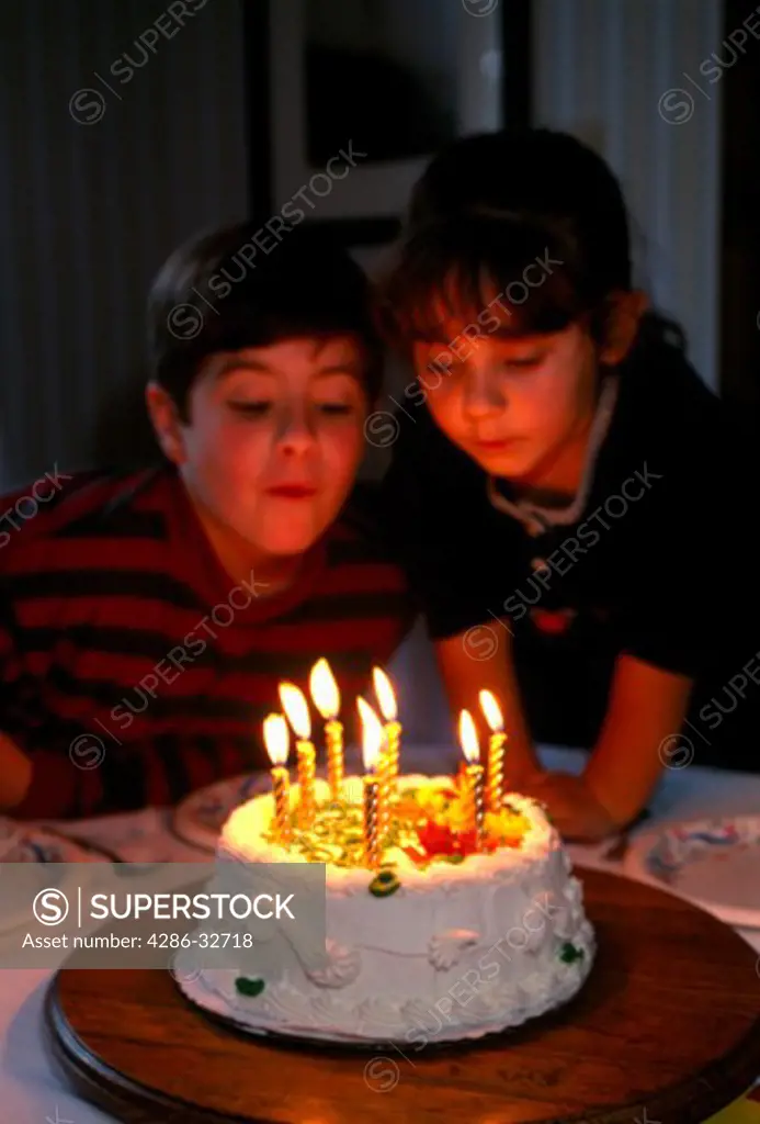 Brother and sister blowing out candles on birthday cake