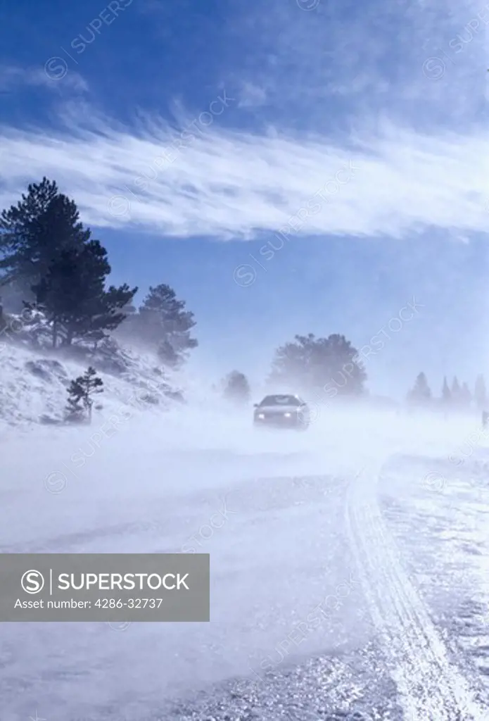 Car traveling on icy road with wind blowing snow, Rocky Mountains.