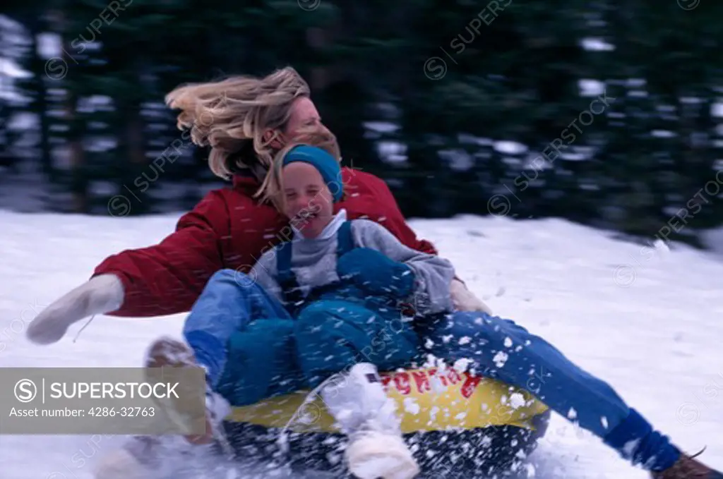 Mother and pre-teen daughter riding on a snow tube with the wind in their hair, with blurred effect.