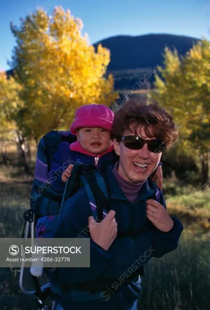 Portrait of a mother carrying her baby daughter on her back while hiking in the Rocky Mountains in the fall.