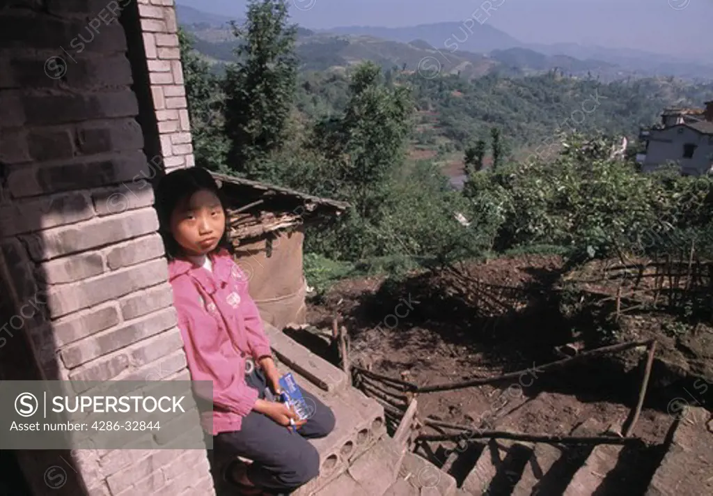 A young girl sits outside her home above a fertile valley near Shibaozhai China