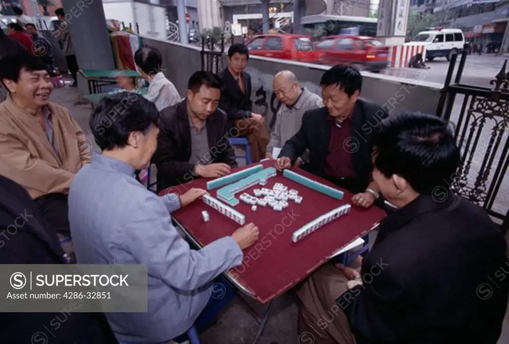 Men playing game of mahjong in outdoor park near busy street in Wanxian China city morning