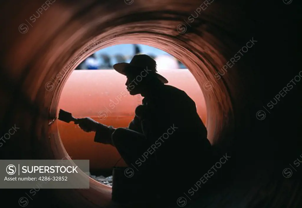 Man painting inside of huge orange drain or water pipe laborer industry city of Fengjie China Asia evening