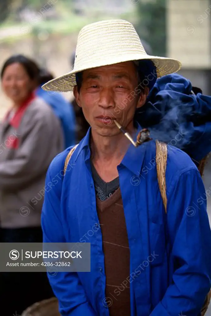 Man smoking pipe in rural market; portrait; wide-brim straw hat; small agrarian village near Wuxi, China, Asia; 042503