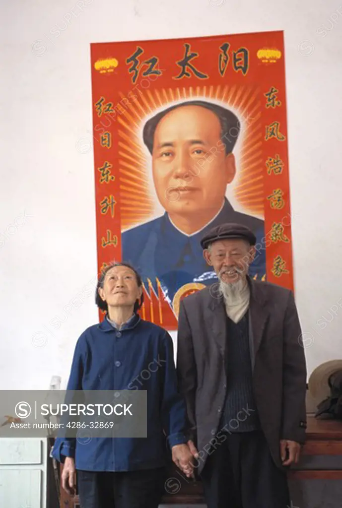 An indoor portrait of a senior Chinese couple in front of a poster of Chairman Mao near Zigui China
