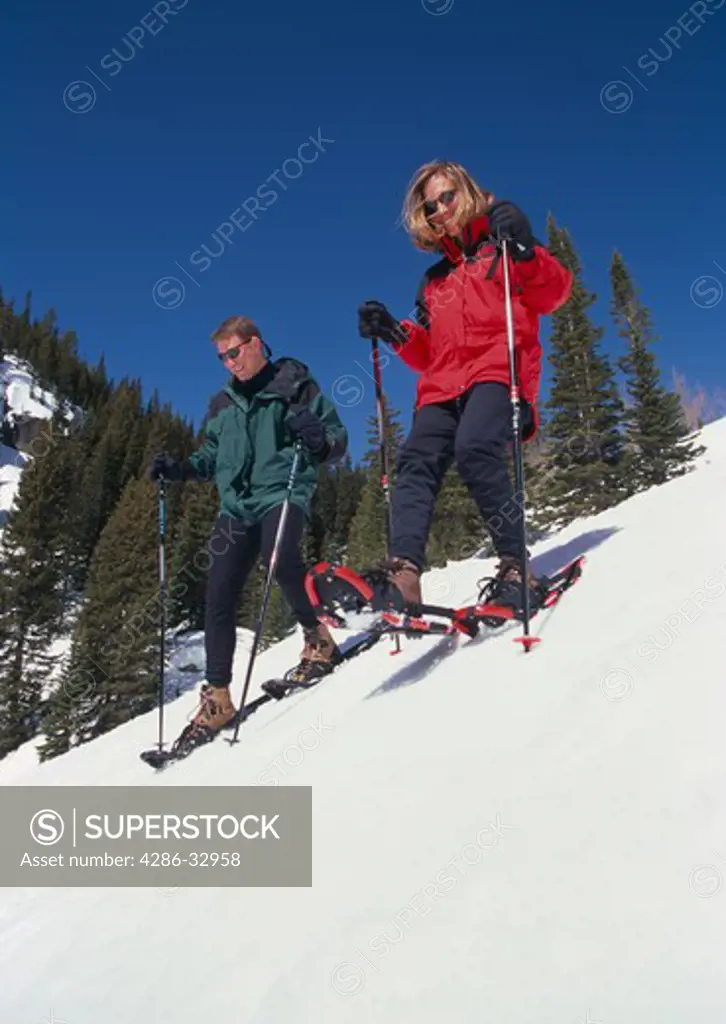Young couple snowshoeing down a steep hill in Rocky Mtns, CO