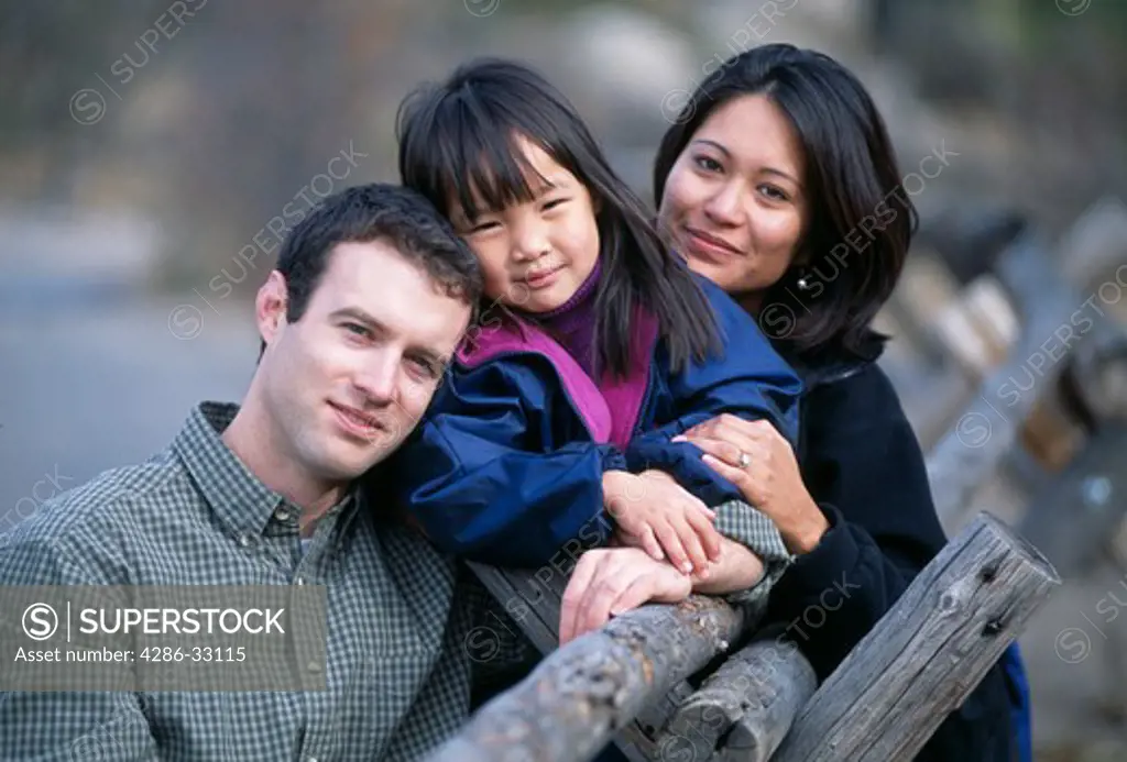 A family of three posing for an outdoor portrait along a wooden fence near Lumpy Ridge, Rocky Mtns, CO