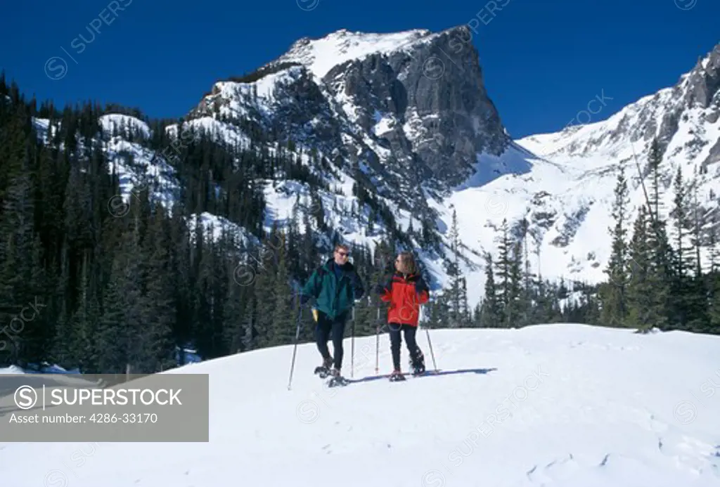Couple snowshoeing with Hallett Peak in background, Rocky Mtn Nat'l Park, CO